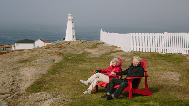 two individuals sitting in red Adirondack chairs overlooking the ocean