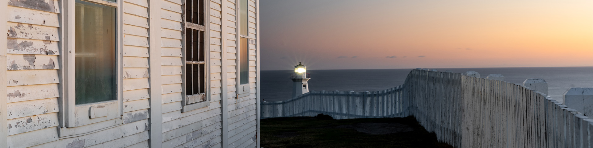 close-up of a white, wooden building overlooking a lighthouse at sunrise.