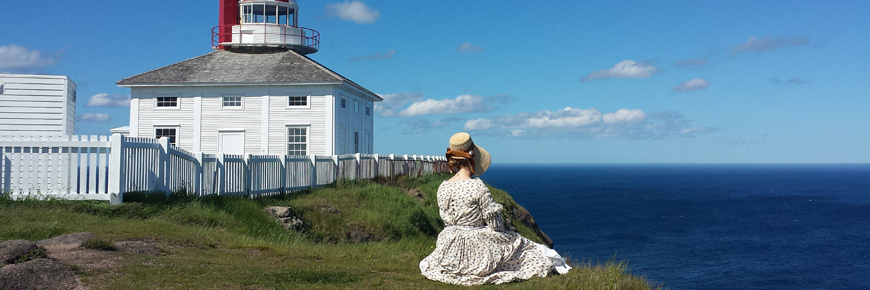 a woman in historic costume sits by the lighthouse overlooking the ocean
