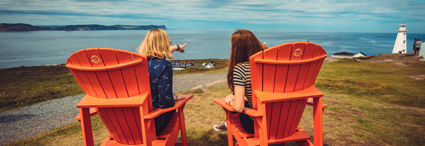 two individuals sitting in red chairs overlooking the ocean and a lighthouse
