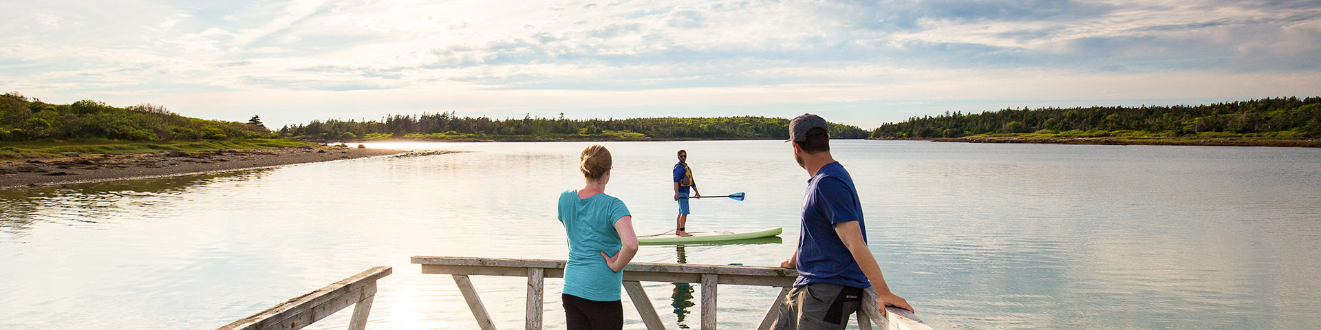  Two people stand on a dock watching someone paddle board while the sunsets