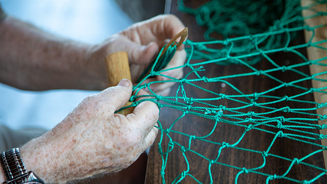 Two hands holding wooden tools while making a green fishing net