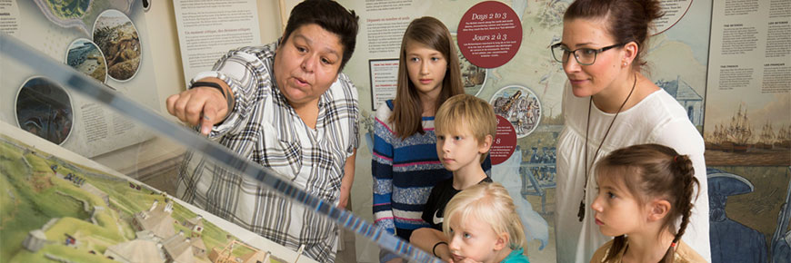 Un groupe de jeunes visiteurs examinent une exposition muséologique sous verre au lieu historique national du Fort-Anne.