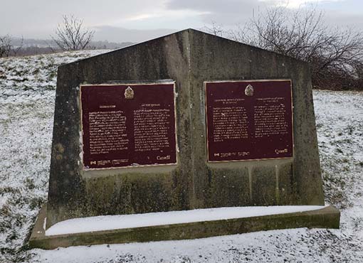 Monument en pierre enneigé avec deux plaques marron.