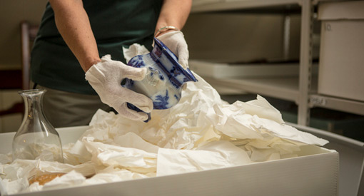 Un interprète de Parcs Canada porte des gants blancs pour manipuler un artefact : un vase bleu et blanc.