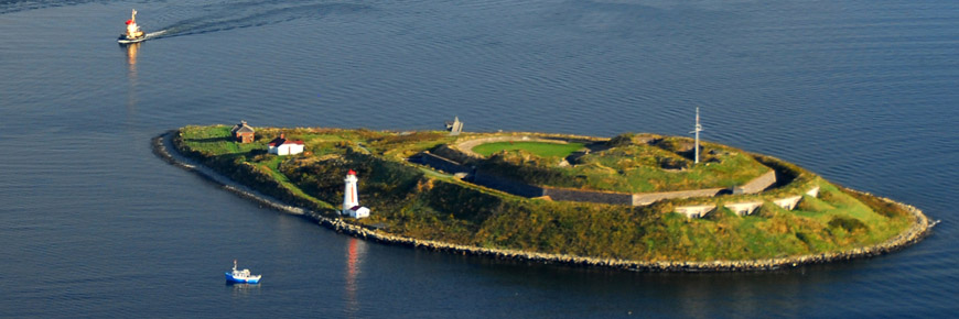 An aerial view of Georges Island and Halifax harbour from Halifax, with a small boat in the foreground and Theodore tugboat in the background. 