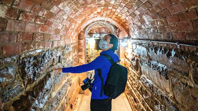 A visitor walking through a bricked tunnel.