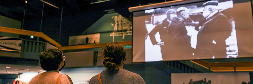 Two people look up at an historical photo of three men displayed on a projector screen