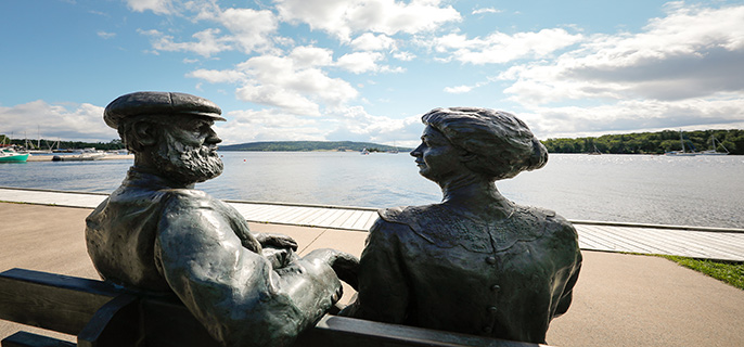Statues of Alexander Graham and Mabel Bell look at one another with the Baddeck Bay in the background