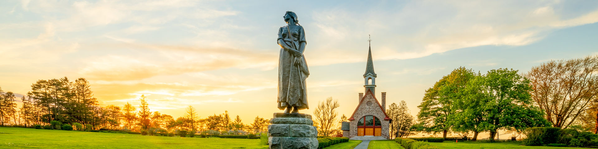 The statue of Evangeline with the Grand-Pré Memorial Church in the background at sunset.