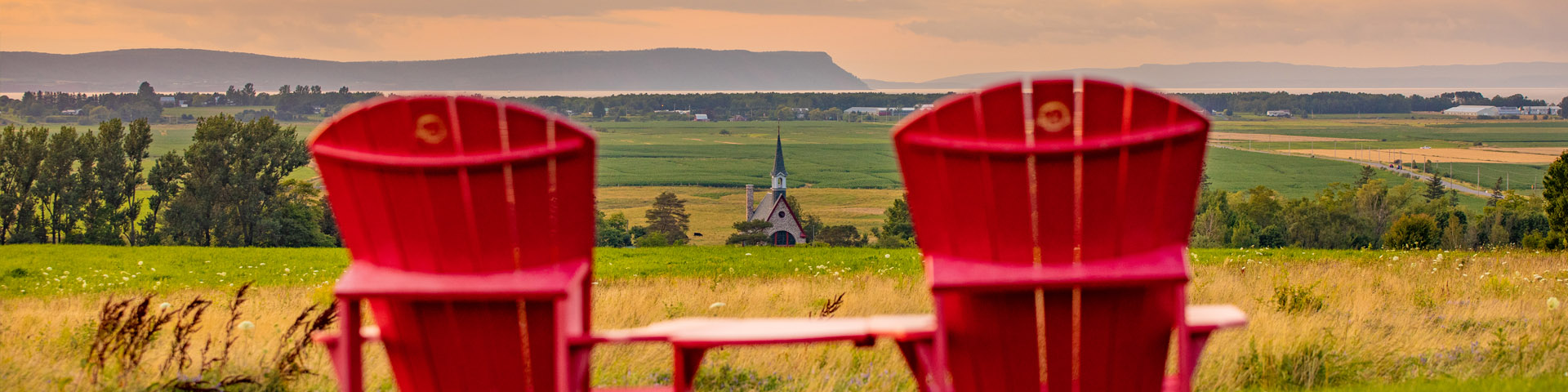 Des chaises rouges offrant une vue sur le paysage de Grand-Pré, avec le cap Blomindon en arrière plan.