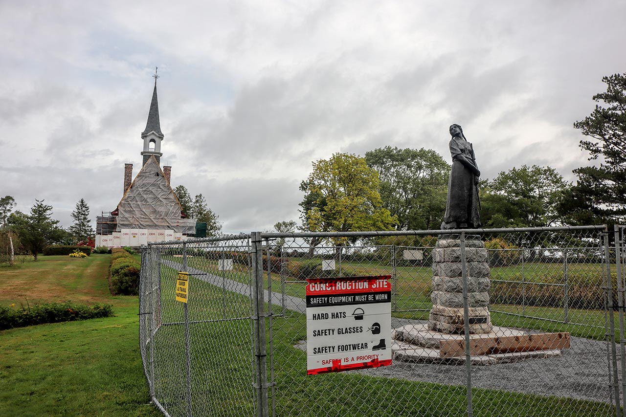The Evangeline statue surrounded by a metal fence with the church in the background surrounded by construction staging.