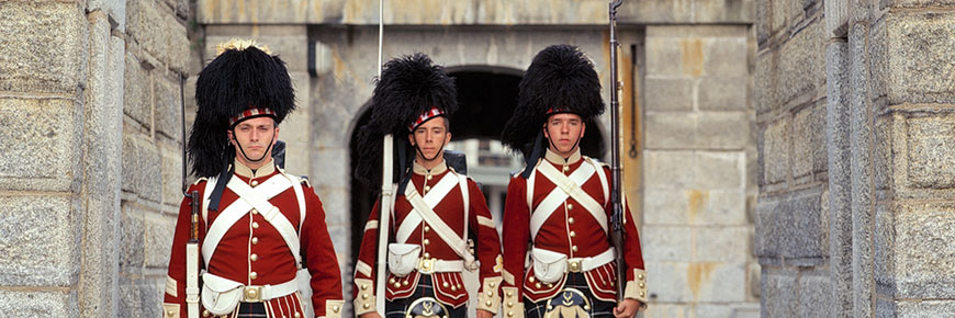 Soldiers in full 78th Highlander uniform, holding rifles and standing next to the wall inside Halifax Citadel National Historic Site.