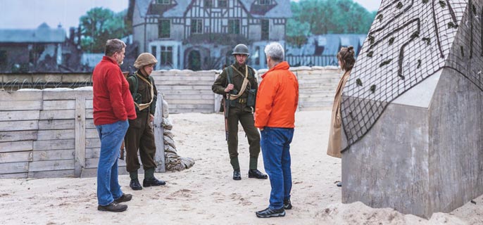 Deux visiteurs et deux soldats sont entourés de barricades de l’exposition « À l’assaut de la plage : Expérience du jour J ».