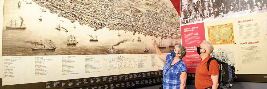 Des visiteurs montrent du doigt une vaste carte historique d’Halifax occupant tout un mur, du plancher au plafond.