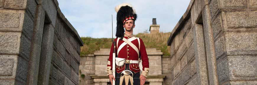 A soldier in full 78th Highlander uniform, holds a rifle and stands next to the wall inside Halifax Citadel National Historic Site. 
