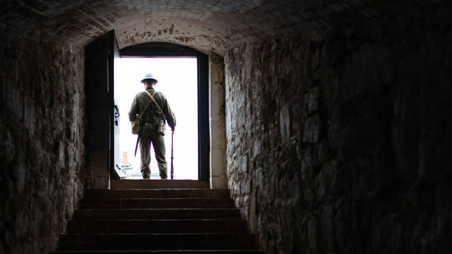Un interprète habillé en soldat de la Seconde Guerre mondiale se tient dans l’embrasure d’une porte.