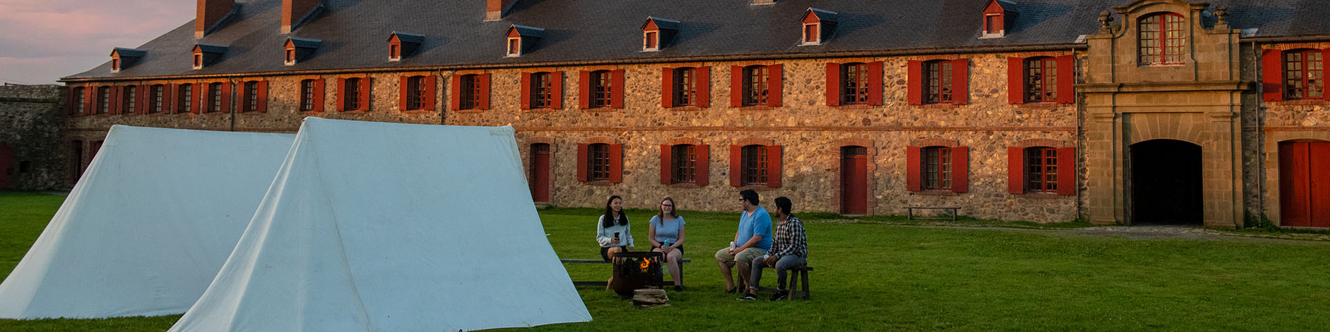 A group of friends sit by a fire next to canvas tents