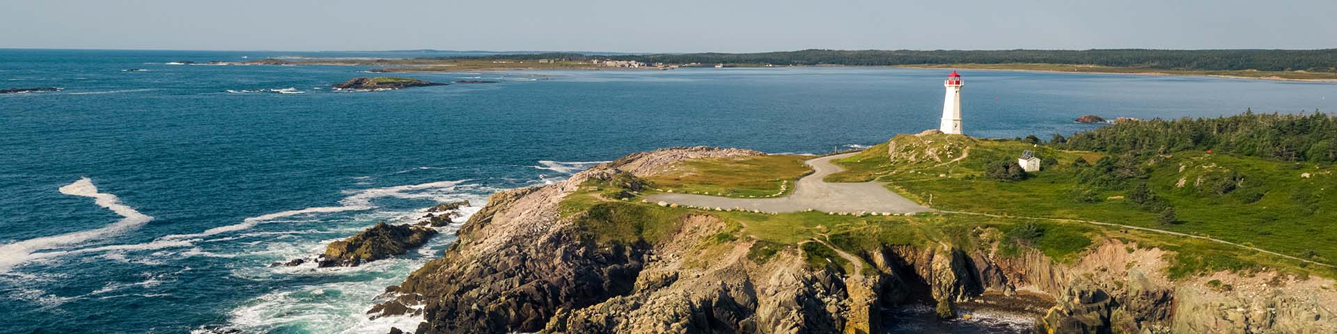 Aerial view of the Louisbourg lighthouse on the ocean with a view of the reconstructed town in the background