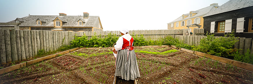 A gardener in 18th century costume stands in one of the heritage gardens.
