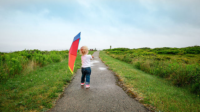 A young child walks on a paved trail holding an umbrella