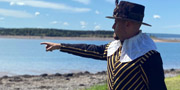 Un interprète, habillé en costume d’époque du Gouverneur comprenant un chapeau et un veste, indique le rivage où les navires sont attendus.