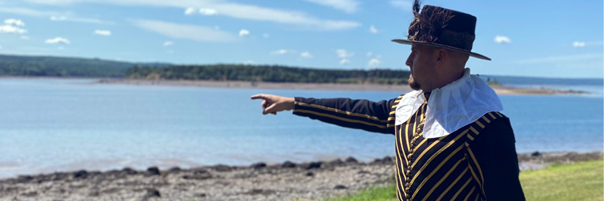 An interpreter dressed as the Governor in period costume including hat and jacket, points to the shore where ships are expected to arrive.