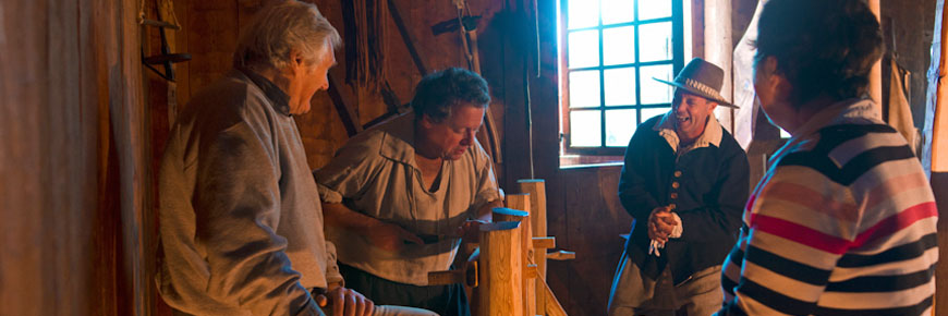 Des visiteurs autour d'un artisan en tournant le bois sur un tour à perche