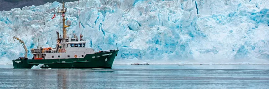 A green and white boat in front of an iceberg.