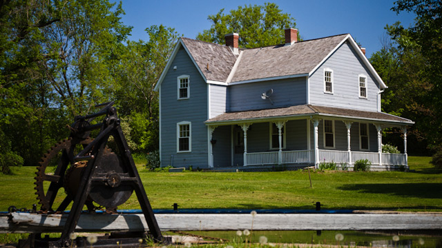 A historic home with a wraparound porch on a sunny day with a lock mechanism visible in the foreground