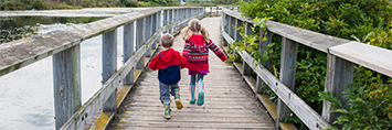 Two children running on a boardwalk.