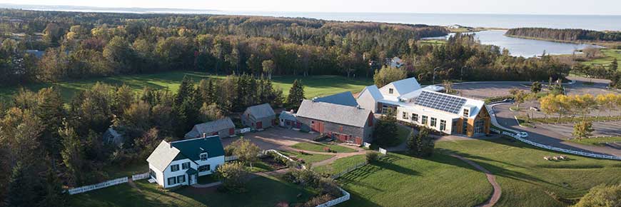 An aerial image of Green Gables Heritage Place in summer showing the Green Gables House, the Visitor Centre, and the surrounding green rolling hills. 