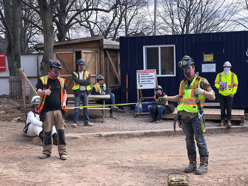 Group of workers in reflective vest standing spaced out. 