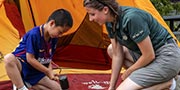 A smiling Parks Canada instructor helps a young boy set up a tent as part of the introduction to camping activity.