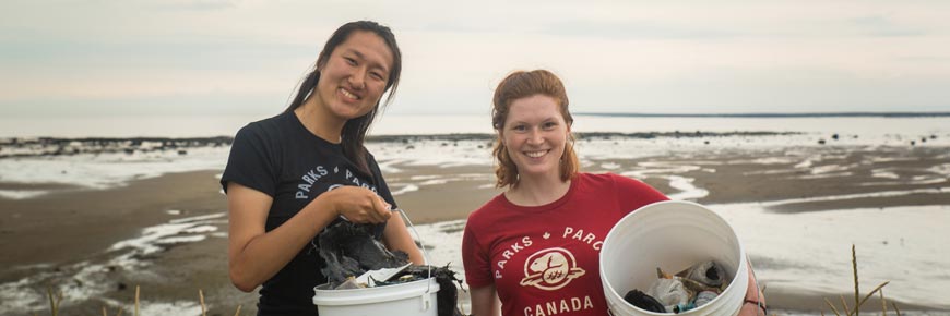 Two smiling participants proudly display the trash they collected in plastic buckets