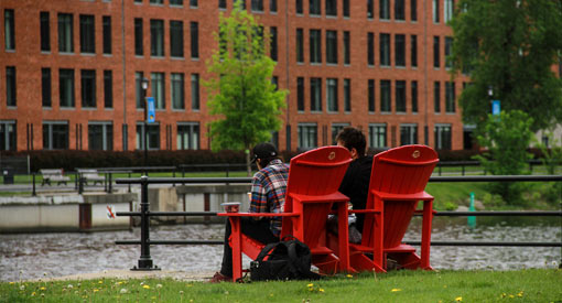 Deux personnes assises sur des chaises rouges à la place des bassins au bord du canal de Lachine 