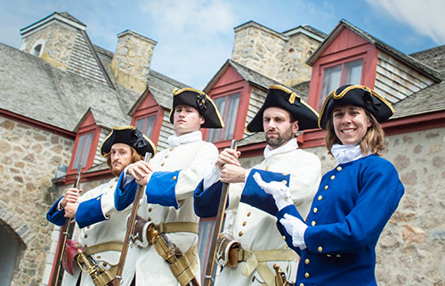 Trois soldats sérieux de Nouvelle-France et une guide souriante costumée