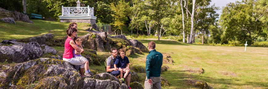 Parents et enfants écoutant un guide de Parcs Canada lors d'une visite guidée du cimetière irlandais.