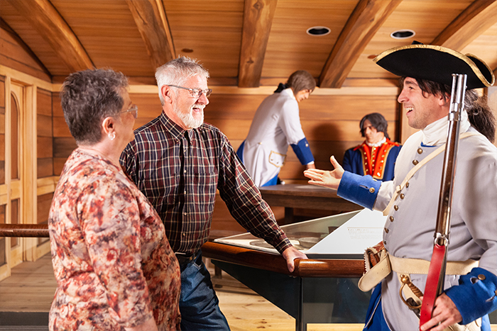Two visitors on the left chatting with an interpreter dressed as a French soldier of the 18th century in one of the rooms reconstructing the interior of the council room aboard the frigate, Le Machault. 