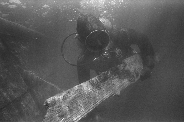 Black and white photo of a diver holding a piece of wood in his hands.