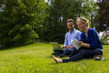 A happy couple using a laptop, sitting on the lawn