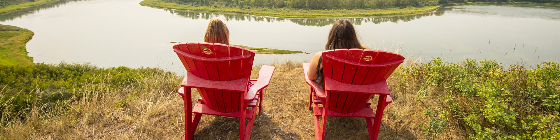 Two visitors sit Parks Canada red chairs overlooking the river
