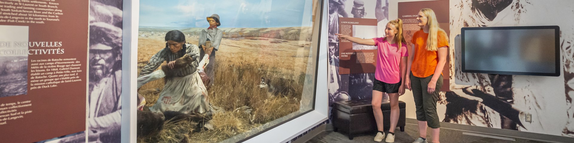 Deux visiteuses debout au musée regardent le diorama d’abattage de bisons.