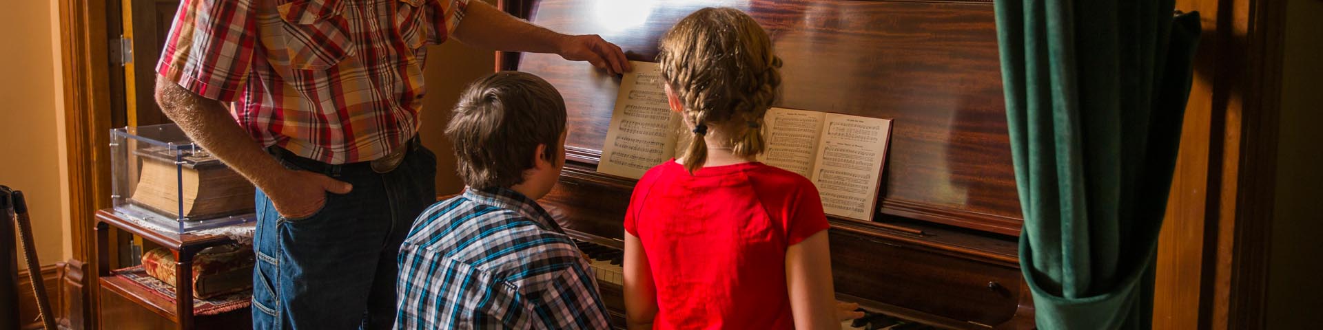  A family is learning about the piano music played in the stone house at Motherwell Homestead