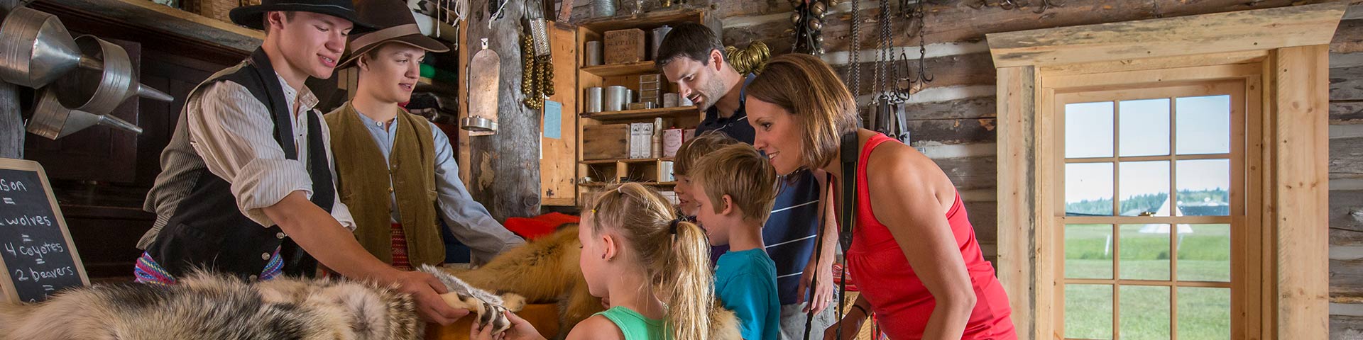 A family checking out the wares in the Métis trading cabin with the help of a couple of costumed interpreters at Fort Walsh National Historic Site.
