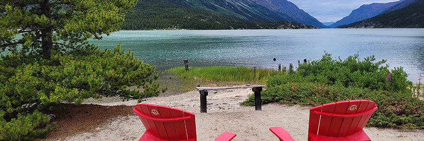 red adirondack chairs facing a lake with mountains in the background