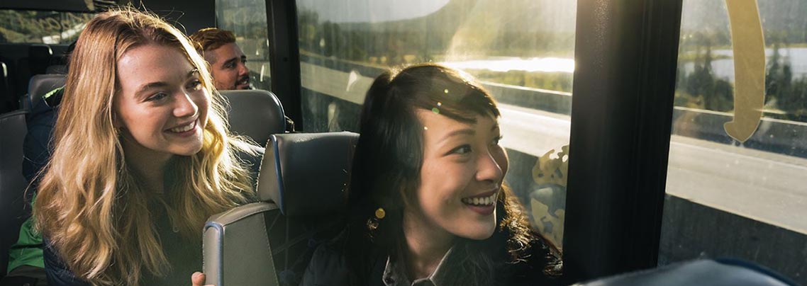 Smiling passengers on a bus with the sun setting outside