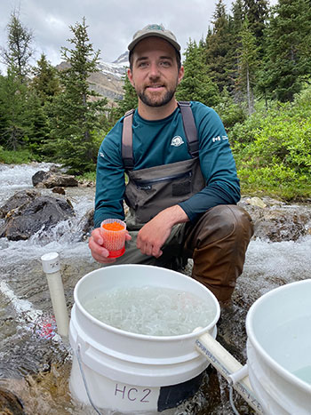 A Parks Canada team member kneels by buckets and pipes that make up the remote streamside incubation. 