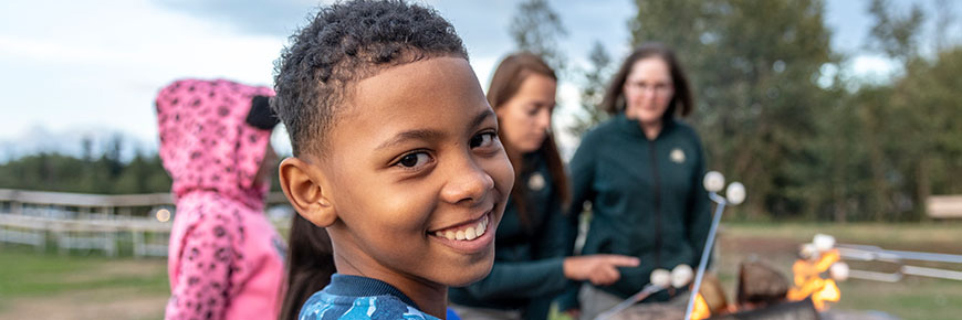 A boy looks at the camera while roasting marshmallows with Parks Canada staff.