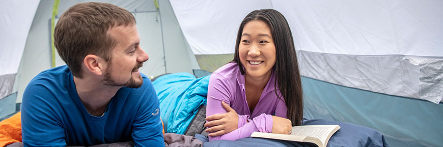 Two campers snuggle up inside their tent with a book.
